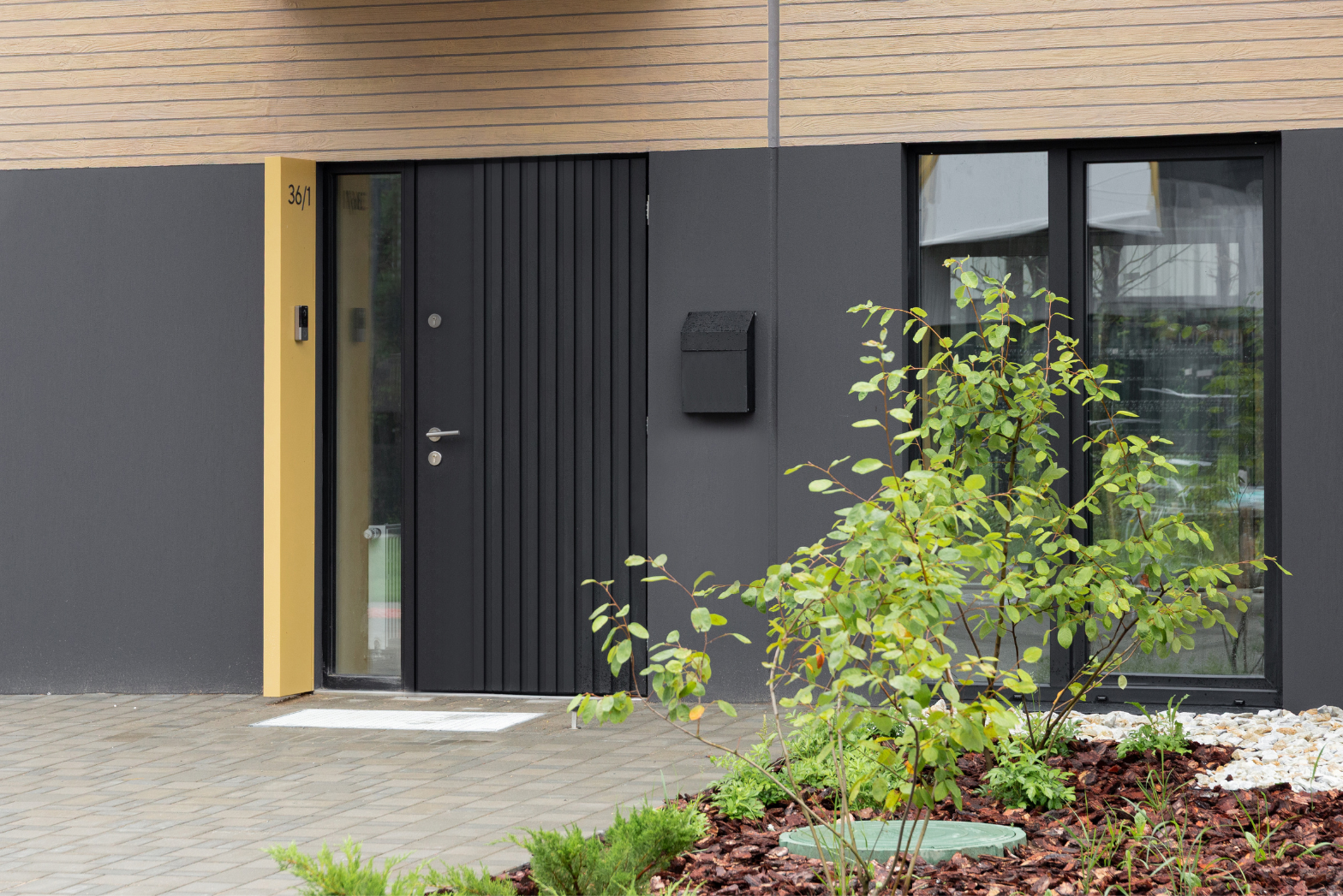 Входные двери в дом чёрные с вертикальной фрезеровкой, серебристой ручкой и почтовым ящиком.