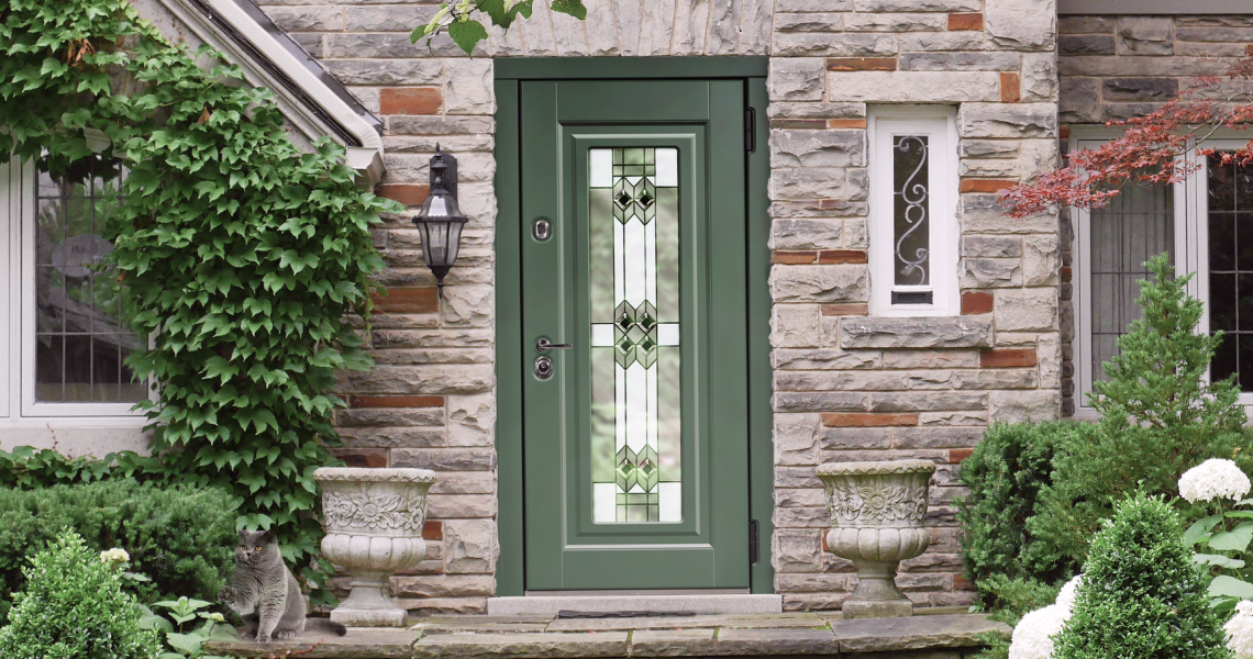 Входная дверь с витражом зеленого цвета с декоративным стеклом встроенная в каменный фасад.