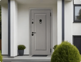 Входные двери для частного дома серые с декоративной фурнитурой на фоне белых стен.