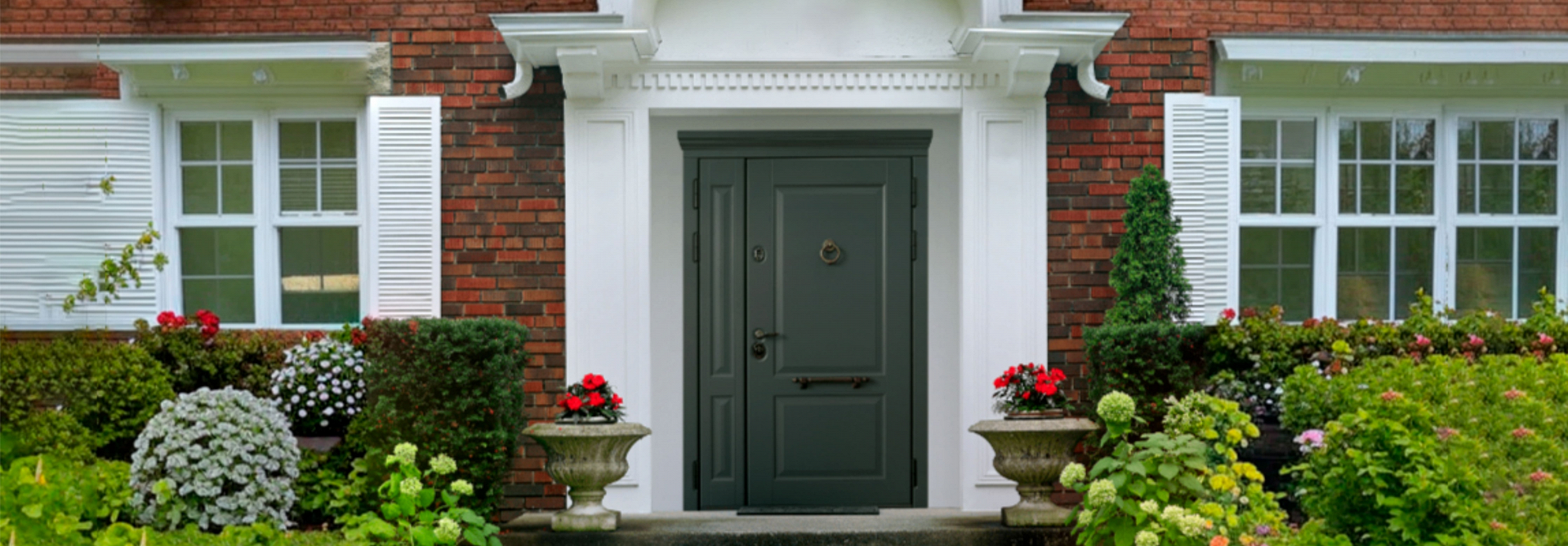 Входные металлические двери на заказ украшают фасад кирпичного дома с белыми рамами.